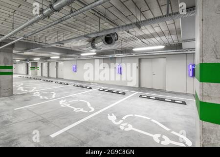 Leere öffentliche Tiefgarage oder Garageninnenraum mit betongestrichenen Säulen und Schildern. Ladestation für Elektroautos. Stockfoto
