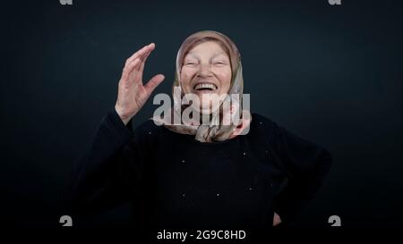 Porträt einer türkischen älteren muslimischen Frau mit schwarzem Hintergrund. Sie ist sehr glücklich und lachend. Stockfoto