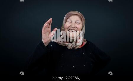 Porträt einer türkischen älteren muslimischen Frau mit schwarzem Hintergrund. Sie ist sehr glücklich und lachend. Stockfoto