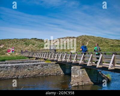 Zwei Spaziergänger überqueren die drei Viertel Meile hölzerne Fußgängerbrücke über den Fluss Bush in der Nähe von Runkerry Beach an der Antrim Causeway Coast Stockfoto