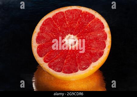 In Scheiben geschnittene, verspiegelte Grapefruit auf schwarzem Hintergrund Stockfoto