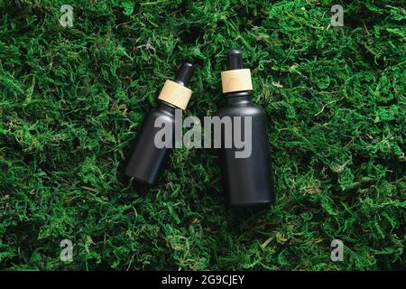 Schwarze Tropferserumflaschen auf Mooshintergrund. Luxus-Kosmetik-Design, Branding. Flach liegend, Draufsicht. Stockfoto