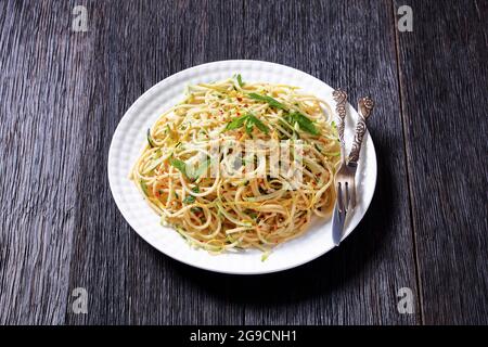 Sommer-Spaghetti alla carrettiera mit Minzblättern, Zitronenschale, Pecorino-Käse, Chilischoten-Flocken, Petersilie und geriebenen Zucchini auf einem weißen Teller Stockfoto