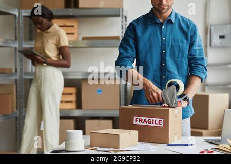 Beschnittenes Porträt eines jungen Mannes, der im Lager Boxen mit zerbrechlichen Aufklebern verpackt und Platz zum Kopieren verwendet Stockfoto