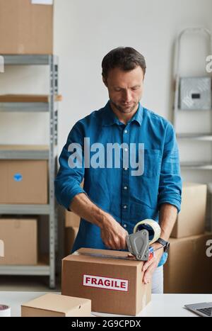 Vertikales Porträt eines jungen Mannes, der im Lager Boxen mit zerbrechlichen Aufklebern verpackt, Platz zum Kopieren Stockfoto