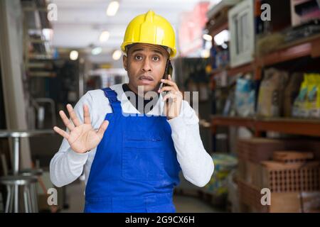 Lateinamerikanischer Mann in blauen Overalls telefoniert im Baumarkt Stockfoto