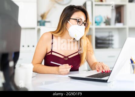 Latina Frau in Gesichtsmaske arbeitet im Büro Stockfoto