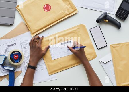 Draufsicht auf weibliche Hände, die Versandschein für Paket über dem Arbeitsplatz beim Lieferservice ausfüllen, Platz kopieren Stockfoto