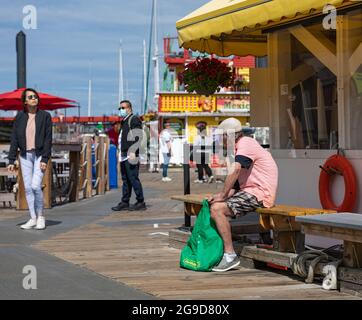 Seitenansicht eines traurigen armen Mannes, der an einem sonnigen Tag auf der Holzbank in Fisherman Wharf Victoria, BC, Kanada, am 23,2021. Juli sitzt. Straßenansicht, Reisefoto Stockfoto