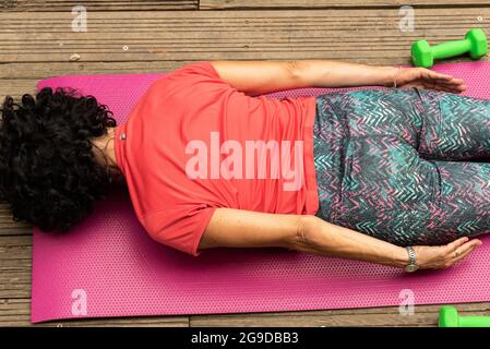 Reife Frau in einem roten Sport-T-Shirt Training Pilates auf einer rosa Matte Stockfoto