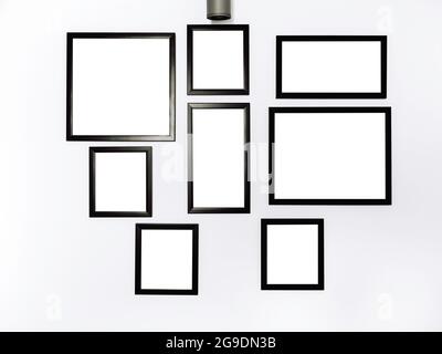 Gruppe von Mockup-Bilderrahmen. Weißes quadratisches Bild mit schwarzem Rahmen-Modell, das auf dem weißen Wandhintergrund hängt. Stockfoto