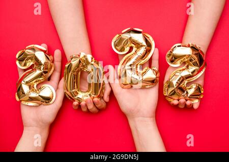 Hände hoch, hält die goldenen Zahlen 2022 von den Kugeln des neuen Jahres in gelber Metallic-Farbe auf einem roten Hintergrund.das Konzept eines glücklichen und gesunden Stockfoto