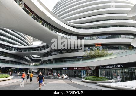 Peking, China. Juli 2021. Menschen, die Gesichtsmasken tragen, gehen in die Nähe des Einkaufszentrums „Galaxy SOHO“ in Peking. Galaxy SOHO liegt in der East 2nd Ring Road, in der Nähe von Chaoyangmen, Peking. Es wurde 2012 fertiggestellt und von Zaha Hadid Architects, Großbritannien, auf einer Fläche von 334000 Quadratmetern (3595000 Quadratfuß) gebaut. Kredit: SOPA Images Limited/Alamy Live Nachrichten Stockfoto