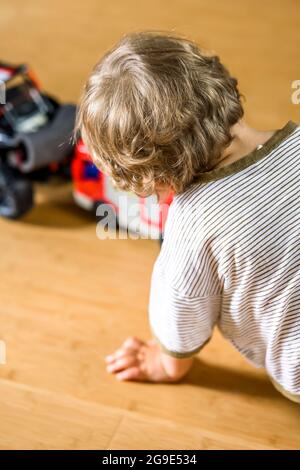 Ein kleiner lockiger Junge spielt begeistert mit einem Spielzeugauto und kleine Männer stellen sich mit der Participatio kindisch eine reale Lebenssituation vor Stockfoto