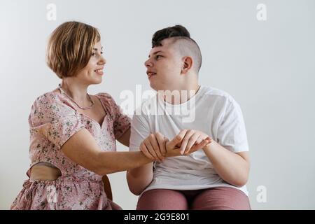 Mutter umarmt behinderten Jungen 17 Jahre alt im Rollstuhl mit zerebraler Lähmung auf weißem Hintergrund. Frau hilft Person mit besonderen Bedürfnissen. Emotional Stockfoto