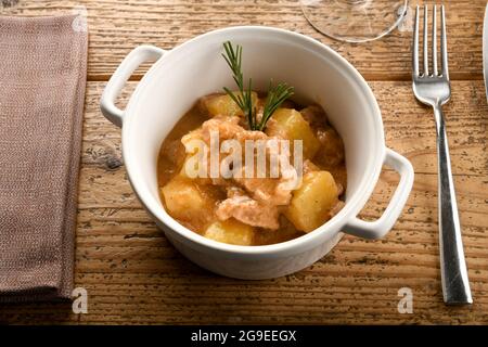 Von oben Keramikschale mit leckerem italienischem Kalbseintopf mit Kartoffeln und Rosmarin in der Nähe von Gabel und Serviette auf Holztisch gelegt Stockfoto