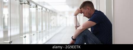 Frustrierter, müder Mann sitzt im Flur unter der Tür Stockfoto