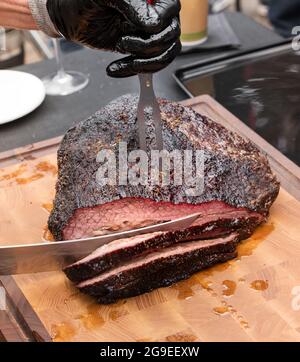 Der Koch schnitzt eine Portion saftig mariniertes, würziges Rinderbrisket auf einem Holzschneidebrett in einem hohen Winkel aus nächster Nähe auf der Messerklinge Stockfoto