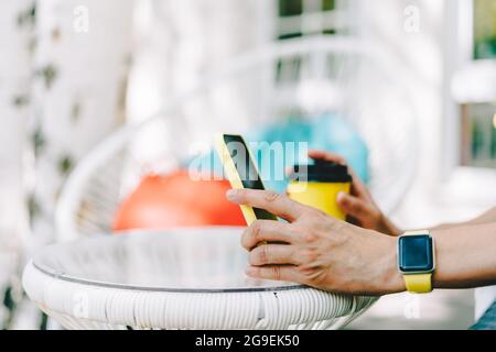 Aus Frauenhänden, die ein gelbes Mobiltelefon mit leerem Bildschirm halten. Digitales Mobiltelefon mit Mock-up. Frau sitzt Café Restaurant und Stockfoto