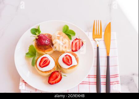 Süße Pfannkuchen mit Cottage-Käse auf dem Teller, serviert mit Erdbeeren. Russische Syrniki-, Ricotta- oder Quark-Krapfen Stockfoto