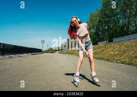 Eine Frau mit rosafarbenen Haaren fährt auf Rollschullauffahrten auf der Straße. Stockfoto