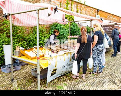 Eine Frau, die auf einem Bauernmarkt in der ummauerten Rose Garden Wynyard Hall einen Stand hat und Cupcakes und andere Süßwaren serviert Stockfoto