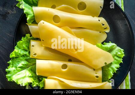 Hartkäse mit großen Löchern auf einem Teller mit Salatblättern geschnitten Stockfoto