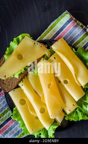 Hartkäse mit großen Löchern auf einem Teller mit Salatblättern geschnitten Stockfoto