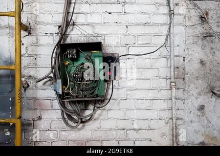 Alte elektrische Schalttafel an der Wand des Hauses. An der weißen Ziegelwand des alten Hauses ragen Elektrokabel aus der elektrischen Zentrale heraus Stockfoto