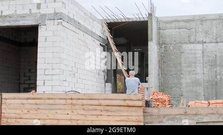 Baustelle mit Arbeitern. Moderne Gebäude im Bau hinter einem Holzzaun. Bauarbeiten. Monolithisches einstöckiges Gebäude aus C Stockfoto