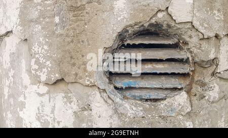 Lüftungsloch in Beton. Runder Lüftungsdeckel aus Metall für die Industrie. Rostiger und schmutziger alter runder Lüftungsrahmen mit horizontalen Metallstreifen Stockfoto
