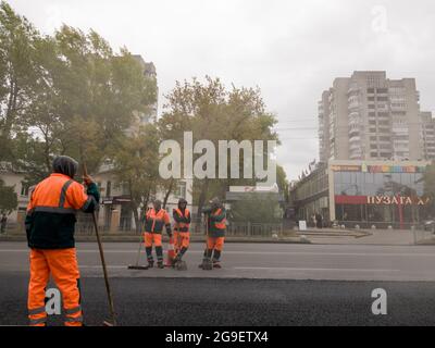 Ukraine, Kiew - 22. September 2019: Arbeiter in orangefarbener Uniform legen Asphalt auf einer Stadtstraße. Straßenmaschinen. Stadtwirtschaft. Arbeiter legt Asphat Stockfoto