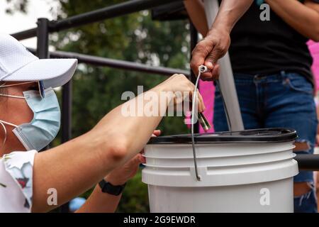 Quelle: Allison Bailey / Alamy Live NewsWashington, DC, USA, 25. Juli 2021. Im Bild: Ein Mitglied der CODEPINK sammelt Spenden bei einer Kundgebung zur Feier der Ankunft von Puentes de Amor (Bridges of Love)-Marschern, die 1300 Meilen von Miami nach Washington, DC, gelaufen sind und die USA aufforderten, ihre Blockade von Kuba zu beenden. CODEPINK hat kürzlich 500 000 Milliarden für den Kauf von 6 Millionen Spritzen für das kubanische Volk zur Bekämpfung von Covid-19 gesammelt und auf der Kundgebung Spenden für Medikamente und medizinische Hilfsgüter angenommen, um die gesundheitlichen Auswirkungen der US-Blockade abzustumpfen. Kredit: Allison Bailey / Alamy Live Nachrichten Stockfoto