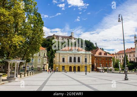 Ljubljana, Slowenien - 15. Juli 2017: Philharmonisches Gebäude auf dem Kongressplatz mit der Burg von Ljubljana im Hintergrund Stockfoto