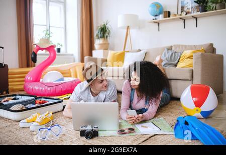 Junges Paar mit Laptop-Verpackung für den Sommerurlaub zu Hause, reden. Stockfoto