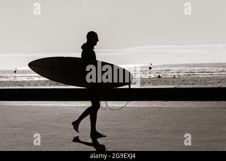 Die Silhouette des Surfers war an der Strandpromenade nicht zu erkennen und ging zum Surfen im Meer. Stockfoto