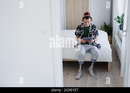 Porträt eines behinderten jungen Mannes, der zu Hause ein Tablet auf dem Bett benutzte, Beinprothetik. Stockfoto