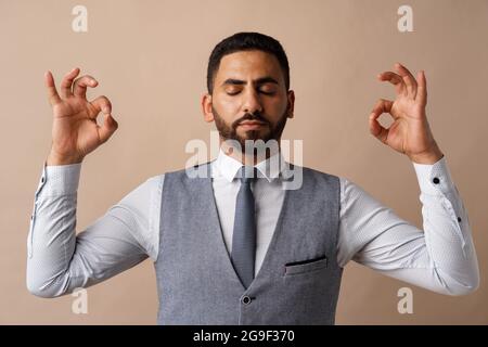 Arabischer Geschäftsmann, der in Zen-Pose steht und vor beigem Hintergrund meditiert Stockfoto