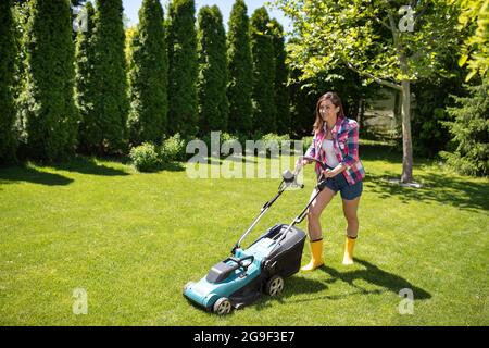 Attraktive Mädchen arbeiten im Garten Trimmen Gras in Sonnenschein. Gärtner mit Rasenmäher im Hof im Sommer. Stockfoto