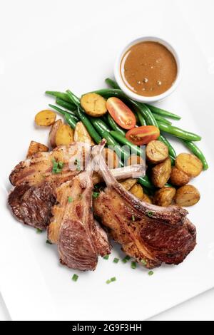 australische Lammkoteletts aus biologischem Anbau mit Gemüse und Soße auf weißem Hintergrund Stockfoto
