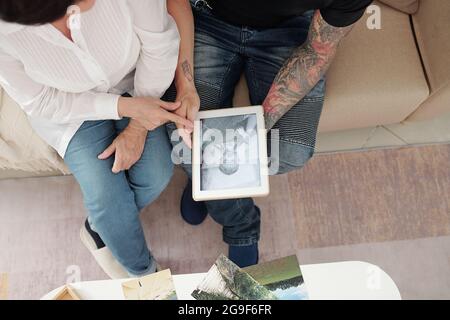Die Mutter zeigt ihrem Sohn sein altes Foto, während sie auf dem Sofa im Zimmer sitzt Stockfoto
