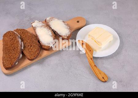 Frisch gebackenes, handwerklich geschnittenes Brot mit Butter und Holzmesser auf Holzschneidebrett Draufsicht, Stockfoto