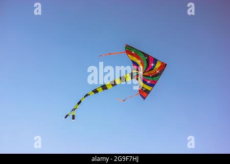 Ein farbenfroher Drachen fliegt im Wind hoch am Himmel. Unterhaltung für Kinder, Spaß im Freien für Kinder im Sommer. Ein Konzept der Freiheit, j Stockfoto