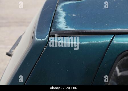 Verblasste Fahrzeugfarbe - abblätternde Lackoberfläche in einem 15 Jahre alten kompakten grünen Auto. Die Farbe ist von der Sonne abgewohnt. Stockfoto