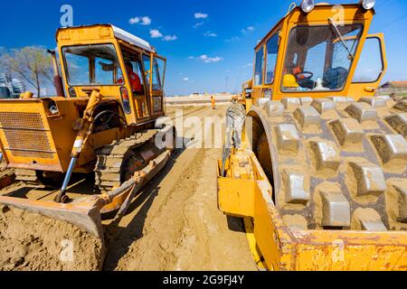Straßenwalze mit Spikes und Bulldozer verdichten, nivellieren Sand für Straßenfundament auf der Baustelle. Stockfoto