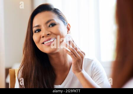 Fröhliche, schöne junge Frau, die Puder auf ihr Gesicht auflegt, um Make-up zu machen Stockfoto