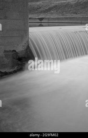 Künstlicher Wasserfall in einem städtischen Betonkanal. Schwarzweißfotografie mit Langzeitbelichtung. Stockfoto