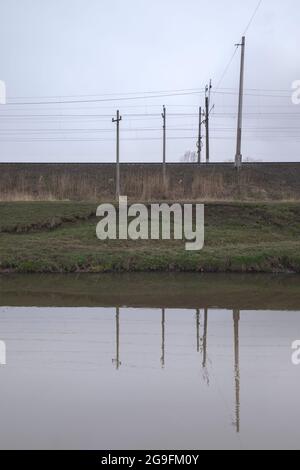 Kanal für die Entwässerung von Wasser in der Nähe einer Eisenbahnschienen. Fuzzy-Reflexion im Wasser. Stockfoto