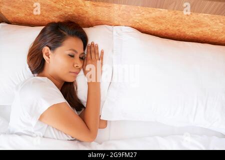 Junge Frau, die alleine auf ihrem bequemen Bett schläft, Blick von oben Stockfoto