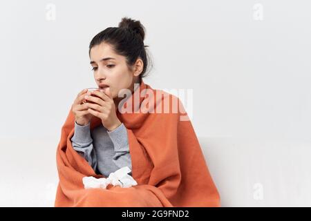 Eine Frau sitzt auf der Couch zu Hause, bedeckt mit einer Decke und trinkt Tee kalt Stockfoto